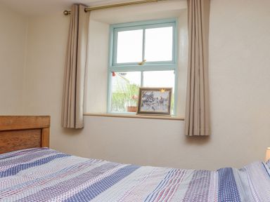 A bedroom with a wooden bed against a wall under a window with beige curtains and a framed picture on the windowsill at Cob Cottage Kilmore County Wexford