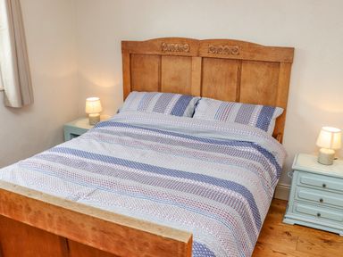A bedroom with a wooden bed and striped bedspread with two bedside lamps on pale blue nightstands at Cob Cottage in Kilmore County Wexford