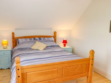 A bedroom with a wooden double bed two bedside tables with lamps and light-colored walls at Cob Cottage Kilmore County Wexford
