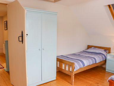 A bedroom with a wooden bed, blue and white striped bedding, a light blue wardrobe and a small light blue nightstand at Cob Cottage in Kilmore County Wexford