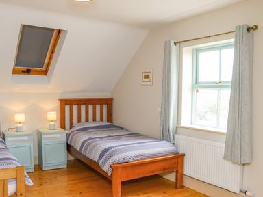 A bedroom with two wooden single beds two bedside tables with lamps a skylight and a window with curtains at Cob Cottage in Kilmore County Wexford