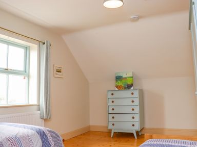 A bedroom with two beds a window with curtains a chest of drawers and a painting on top at Cob Cottage in Kilmore County Wexford