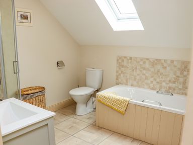 A bathroom with a bathtub, toilet, sink, laundry basket, and skylight at Cob Cottage in Kilmore County Wexford