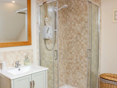 A bathroom with a glass shower enclosure a tiled shower wall a sink with a cabinet and a mirror above it at Cob Cottage Kilmore County Wexford