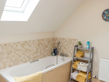 A bathroom with a bathtub under a skylight and a shelf with towels and toiletries at Cob Cottage Kilmore County Wexford
