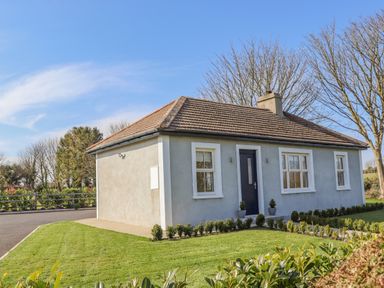 A single-story house with three windows and a central door surrounded by grass and small bushes at An Teachain in Adamstown County Wexford