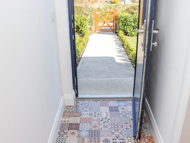 A view of an open door with patterned tiles inside and a pathway leading to a wooden gate outside at An Teachain in Adamstown County Wexford