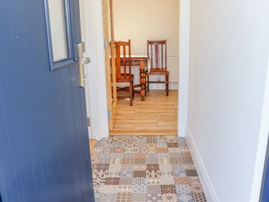 An open blue door leading to a hallway with patterned tile floor and a room with wooden table and two wooden chairs at An Teachain in Adamstown County Wexford