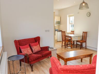 A living room with red upholstered chairs and a wooden table next to a dining table with wooden chairs at An Teachain in Adamstown County Wexford