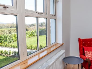 A window with a wooden sill overlooking a garden next to a radiator a small round table and a red armchair at An Teachain in Adamstown County Wexford