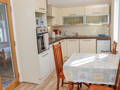 A kitchen with cabinets a sink a stove a microwave and a dining table with chairs at An Teachain in Adamstown County Wexford