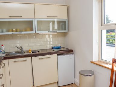 A kitchen area with a sink cabinets a mini fridge a trash bin and a window at An Teachain in Adamstown County Wexford