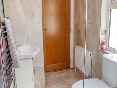 A bathroom with a sink, wooden door, towel on a radiator, toilet, window with a bottle on the sill and tiled walls at An Teachain in Adamstown, County Wexford