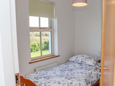 A small bedroom with a single bed next to a window with a view of greenery at An Teachain in Adamstown County Wexford