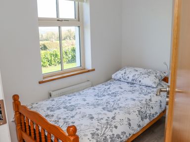 A small bedroom with a wooden single bed next to a window with a view of greenery at An Teachain in Adamstown County Wexford