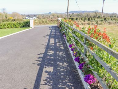 A driveway bordered by a wooden fence with flowers and shrubs at An Teachain in Adamstown County Wexford