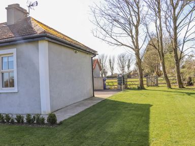 Side view of a house with a lawn small shrubs concrete path trees and a wooden gate at An Teachain in Adamstown County Wexford
