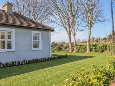 A side view of a house with windows a tiled roof and a garden with grass bushes and trees at An Teachain in Adamstown County Wexford