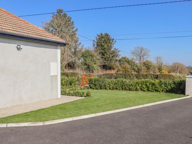 Side of a building next to a grass lawn with a wooden gate and hedges at An Teachain in Adamstown County Wexford
