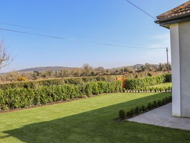 A garden with a lawn and hedges next to a house and hills in the background at An Teachain in Adamstown County Wexford