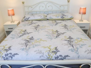 A bedroom with a white metal bed frame and floral bedding two bedside tables with lamps at An Teachain in Adamstown County Wexford
