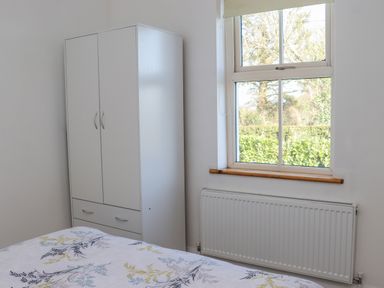 A bedroom with a white wardrobe a window with a view of trees a radiator and a bed with patterned sheets at An Teachain in Adamstown County Wexford