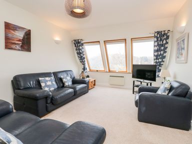 A living room with black leather sofas and armchairs with floral cushions a television and wooden side tables at Rothay in Ambleside