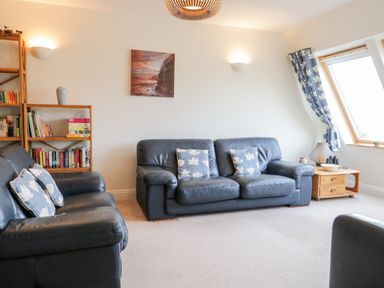 A living room with blue leather sofas a wooden bookshelf and a wooden side table with a window and blue curtains at Rothay in Ambleside