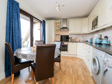 A kitchen with a round dining table and four chairs blue curtains and white cupboards at Rothay in Ambleside