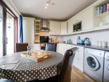 A kitchen with cream cabinets a dining table with polka dot cover and appliances at Rothay in Ambleside