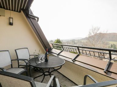 A balcony with a round metal table four chairs a bottle of wine and wine glasses overlooking a hillside at Rothay in Ambleside