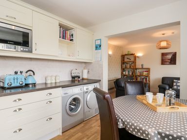A kitchen with washing machines toaster and kettle next to a dining table with cups in Rothay Ambleside