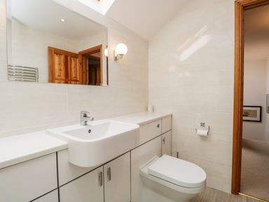 A bathroom with a sink, toilet, large mirror, and wooden door at Rothay in Ambleside