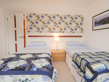 A bedroom with two single beds a nightstand lamp floral wallpaper and a framed picture on the wall at Rothay in Ambleside