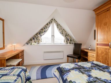A bedroom with two beds a wooden desk a chair a wardrobe and a window with patterned curtains at Rothay in Ambleside