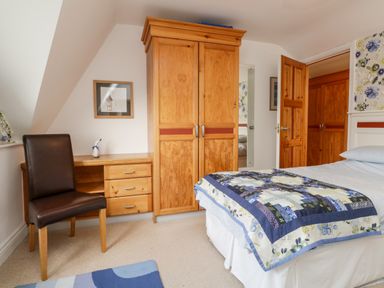 A bedroom with a wooden wardrobe, a desk with drawers, a chair, and a bed with a patterned quilt at Rothay in Ambleside