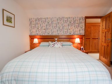 A bedroom with a double bed with plaid bedding two bedside lamps wooden wardrobes and floral wallpaper at Rothay in Ambleside