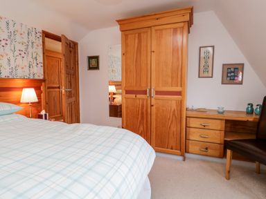 A bedroom with a bed in plaid bedding a wooden wardrobe a wooden desk with drawers a chair and framed pictures on the wall at Rothay in Ambleside