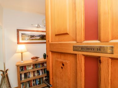 A wooden door with a nameplate reading Rothay 14 opening to a room with a bookshelf a lamp and a framed landscape photo at Rothay in Ambleside