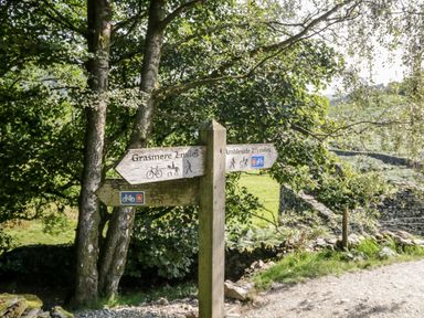 A wooden signpost pointing to Grasmere and Ambleside on a dirt path with trees and stone walls at Rothay in Ambleside