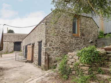 A stone barn with wooden doors and a window surrounded by stone steps and greenery at The Coach House at Thorn Farm Bridford near Moretonhampstead