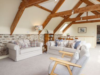 A living room with two sofas, an armchair, wooden beams on the ceiling, and a dining table at The Coach House at Thorn Farm in Bridford near Moretonhampstead