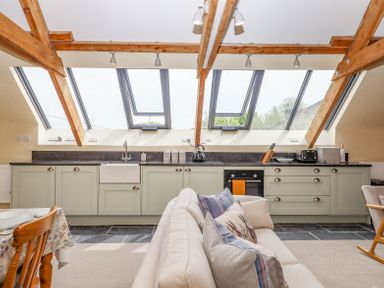 A kitchen with green cabinets and skylight windows behind a beige sofa at The Coach House at Thorn Farm Bridford near Moretonhampstead
