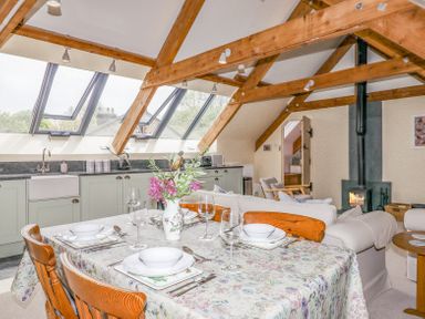 A dining table set with dishes and glasses next to a kitchen with skylights and wooden beams at The Coach House at Thorn Farm in Bridford near Moretonhampstead