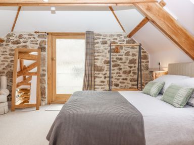 A bedroom with a bed green pillows a freestanding mirror and a door on a stone wall at The Coach House at Thorn Farm Bridford near Moretonhampstead