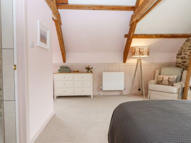 A bedroom with a dresser towels a chair with pillows a floor lamp and exposed wooden beams at The Coach House at Thorn Farm Bridford near Moretonhampstead