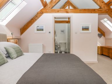 A bedroom with a bed, pillows, wooden beams and an ensuite bathroom visible through an open door at The Coach House at Thorn Farm Bridford near Moretonhampstead