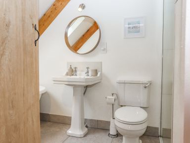 A bathroom with a pedestal sink a round mirror a toilet and a wooden door at The Coach House at Thorn Farm in Bridford near Moretonhampstead