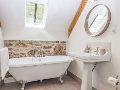 A bathroom with a clawfoot bathtub a pedestal sink a round mirror and a skylight at The Coach House at Thorn Farm Bridford near Moretonhampstead