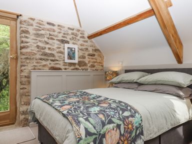 A bedroom with a bed next to a stone wall and wooden door at The Coach House at Thorn Farm Bridford near Moretonhampstead